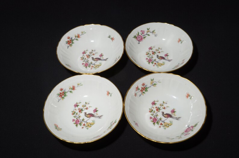 May include: Set of four white porcelain bowls with gold trim and floral designs. Each bowl features a colourful bird and floral pattern.