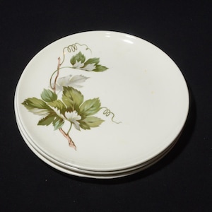 May include: A set of three white ceramic plates with a green vine design. The plates are stacked on top of each other.