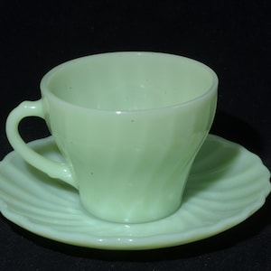 May include: A light green teacup and saucer set. The cup has a curved handle and a spiral design. The saucer has a scalloped edge and a matching spiral pattern. The set is made of glass.