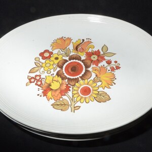 May include: Set of four white ceramic dinner plates with a floral design featuring brown, yellow, orange, and red flowers.