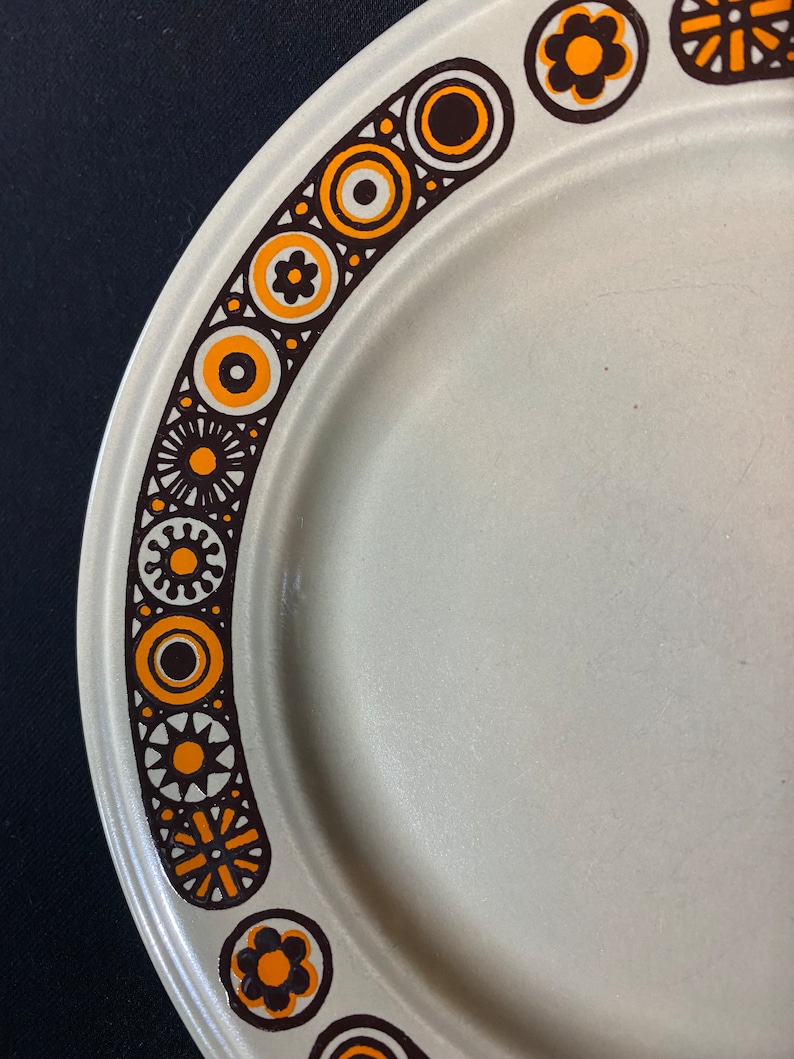 May include: A white ceramic plate with a brown and orange geometric pattern around the edge.