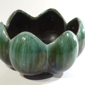 Puede incluir: Un cuenco de cerámica verde y marrón con forma de flor. El cuenco tiene un esmalte verde oscuro con vetas de verde claro y marrón.