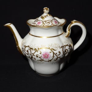 Peut inclure: Théière en porcelaine blanche avec un motif floral doré et rose. La théière a un couvercle et une anse.