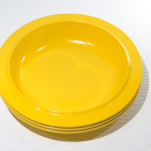 May include: A set of three yellow ceramic bowls. The bowls are stacked on top of each other. The bowls are round and have a slightly raised rim.