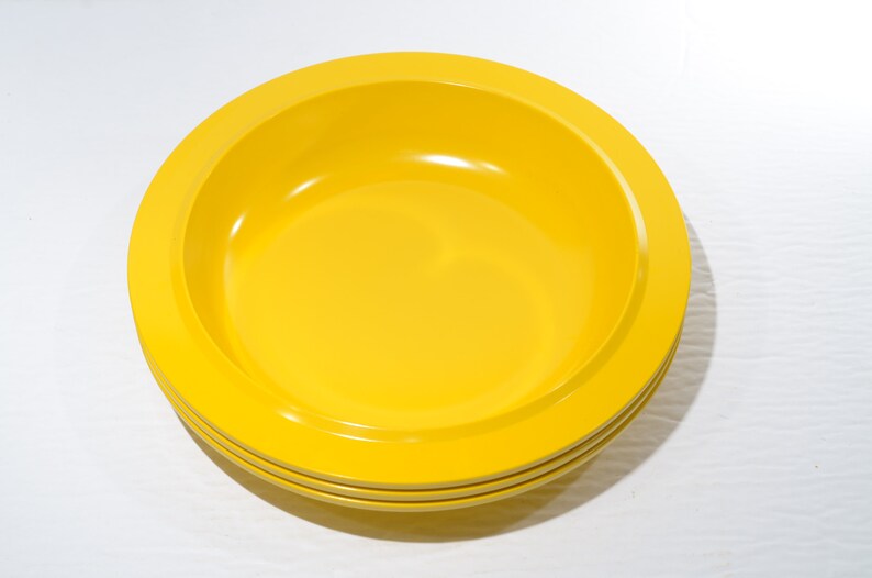 May include: A set of three yellow ceramic bowls. The bowls are stacked on top of each other. The bowls are round and have a slightly raised rim.