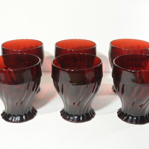 May include: Set of six ruby red glass tumblers with a swirling design. The glasses have a wide base and a rounded top.