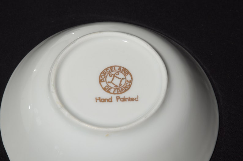 May include: A white porcelain bowl with a gold rim and a gold inscription that reads "Porcelaine de France" and "Hand Painted".