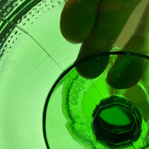 May include: Close-up of the bottom of a green glass bottle with a textured surface and a circular indentation in the center.