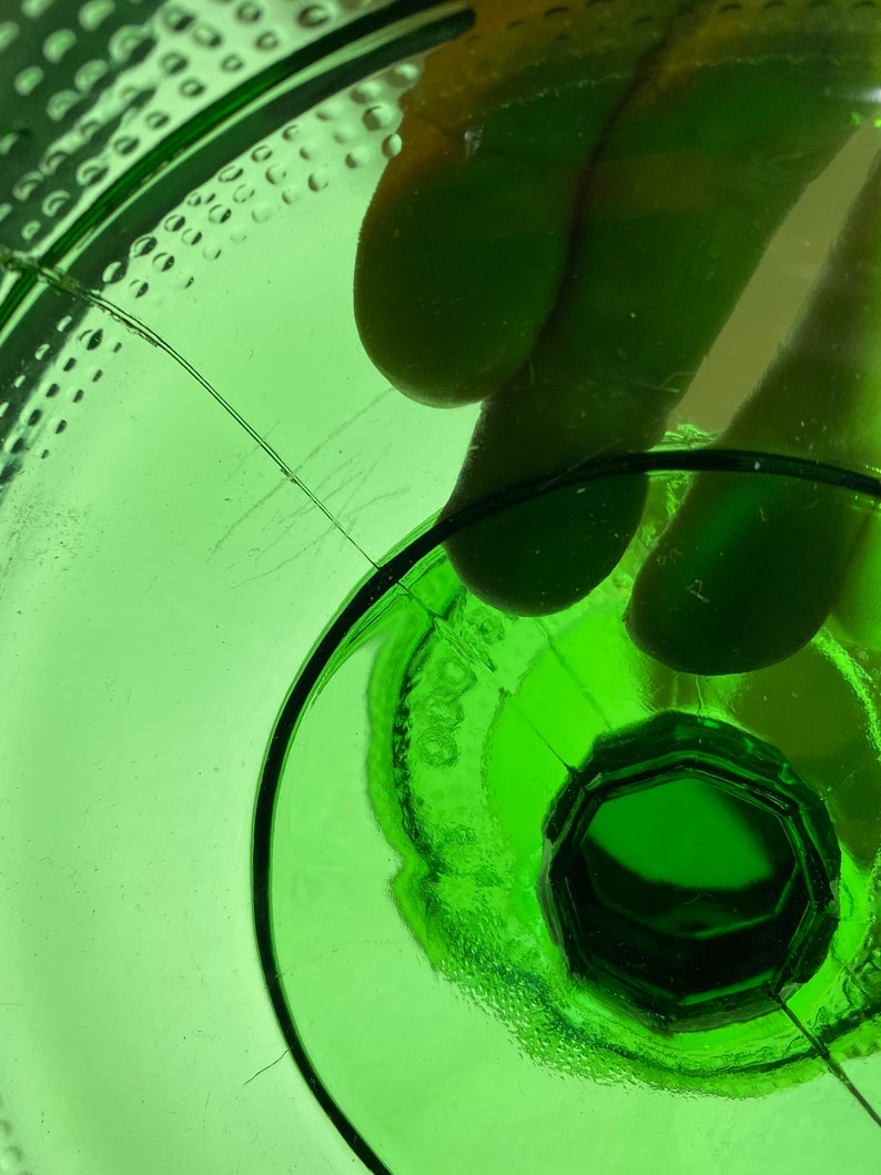 May include: Close-up of the bottom of a green glass bottle with a textured surface and a circular indentation in the center.