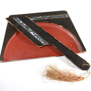 May include: A black and red wooden fan with a mother-of-pearl inlay and a tassel. The fan is closed and the handle is visible.
