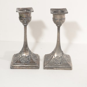 Può includere: Un paio di candelieri d'argento con un design a vite. I candelieri hanno una base quadrata e uno stelo alto e sottile.