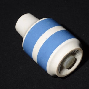 May include: A white ceramic bottle stopper with a blue stripe design. The stopper has a white plastic cap.