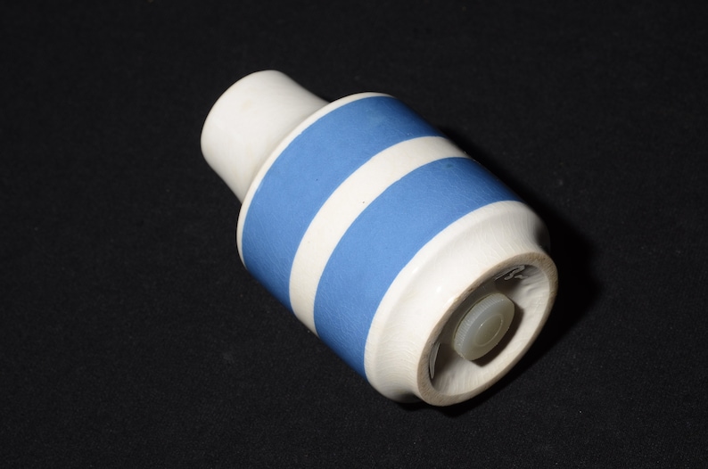 May include: A white ceramic bottle stopper with a blue stripe design. The stopper has a white plastic cap.