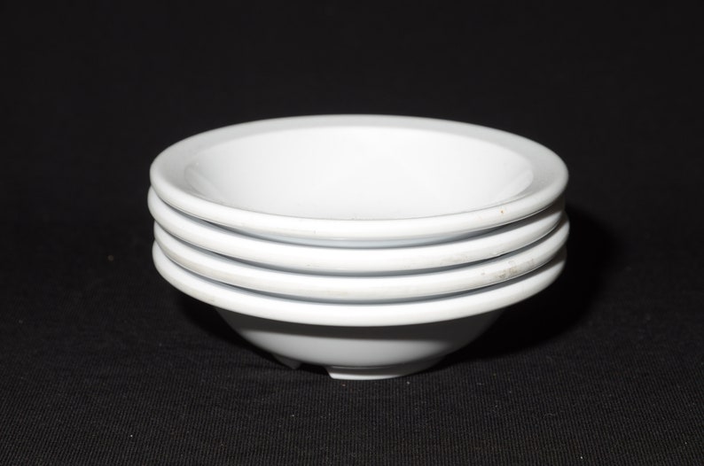 May include: Four white ceramic bowls stacked on top of each other. The bowls are round and have a slight lip.