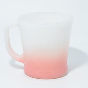Pode incluir: Uma caneca degradê branca e rosa com uma alça curva. A caneca faz a transição do branco no topo para um rosa suave na base. A caneca é de vidro e está vazia.
