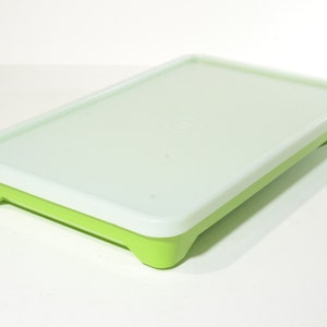 May include: A white rectangular plastic container with a green base and raised edges. The container has a smooth, flat surface and is ideal for storing food.