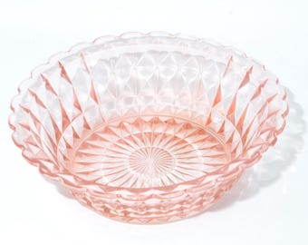May include: A pink glass bowl with a diamond pattern and a scalloped rim. The bowl has a circular design in the center. The glass is transparent, allowing light to pass through, and is set against a white background.