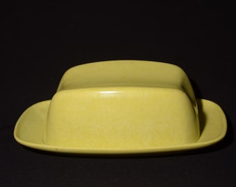 May include: A yellow ceramic butter dish shaped like a hat. The dish has a smooth, rounded top and a wide, flat base.
