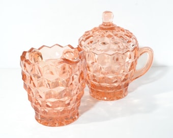 Pode incluir: Um par de travessas de vidro vintage cor de pêssego. Uma é um jarro pequeno com alça e tampa. A outra é uma tigela pequena e aberta. Ambas têm um padrão geométrico em forma de diamante.
