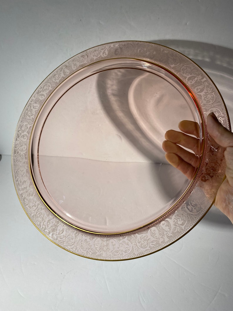Puede incluir: Un plato de servir de vidrio rosa con un borde dorado y un delicado dise&ntilde;o grabado alrededor del borde.