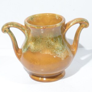 May include: A brown ceramic pitcher with two handles and a green glaze. The pitcher has a rounded body and a wide mouth.