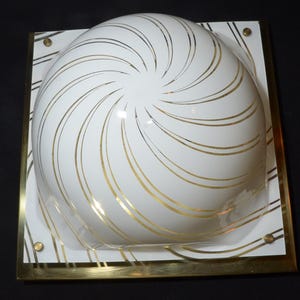 May include: A white ceiling light fixture with a gold metal frame and a white dome-shaped shade with a swirling gold pattern.