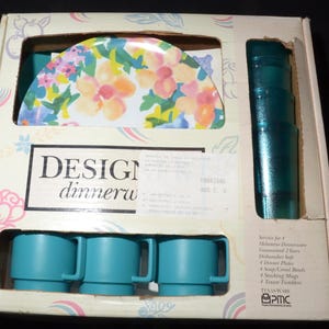 Puede incluir: Una caja de vajilla Design para cuatro personas. El juego incluye cuatro tazas turquesas, cuatro vasos turquesas, cuatro platos de cena con un diseño floral y una jarra turquesa. La caja tiene el texto "Design dinnerware" y "Service for 4".