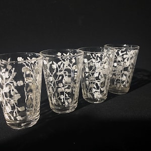 May include: Four clear glass shot glasses with a white floral design.