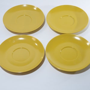 May include: Four yellow ceramic saucers with a slightly raised center.