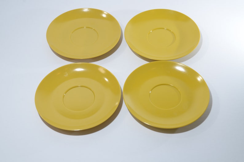 May include: Four yellow ceramic saucers with a slightly raised center.