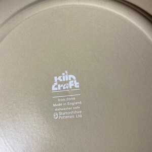 May include: A white ceramic plate with the words "kiln craft" in a stylized font. The plate also has the text "Ironstone Made in England dishwasher safe Staffordshire Potteries Ltd."