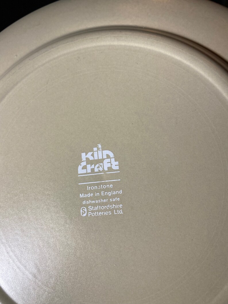 May include: A white ceramic plate with the words "kiln craft" in a stylized font. The plate also has the text "Ironstone Made in England dishwasher safe Staffordshire Potteries Ltd."