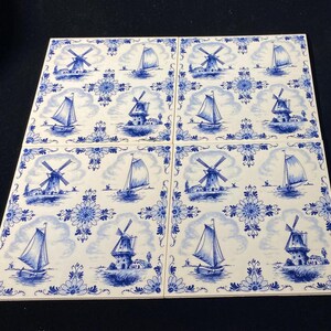 May include: Four square ceramic tiles with a blue and white Dutch design. Each tile features a windmill, sailboat, and floral border. The tiles are arranged together, showcasing the repeating pattern.