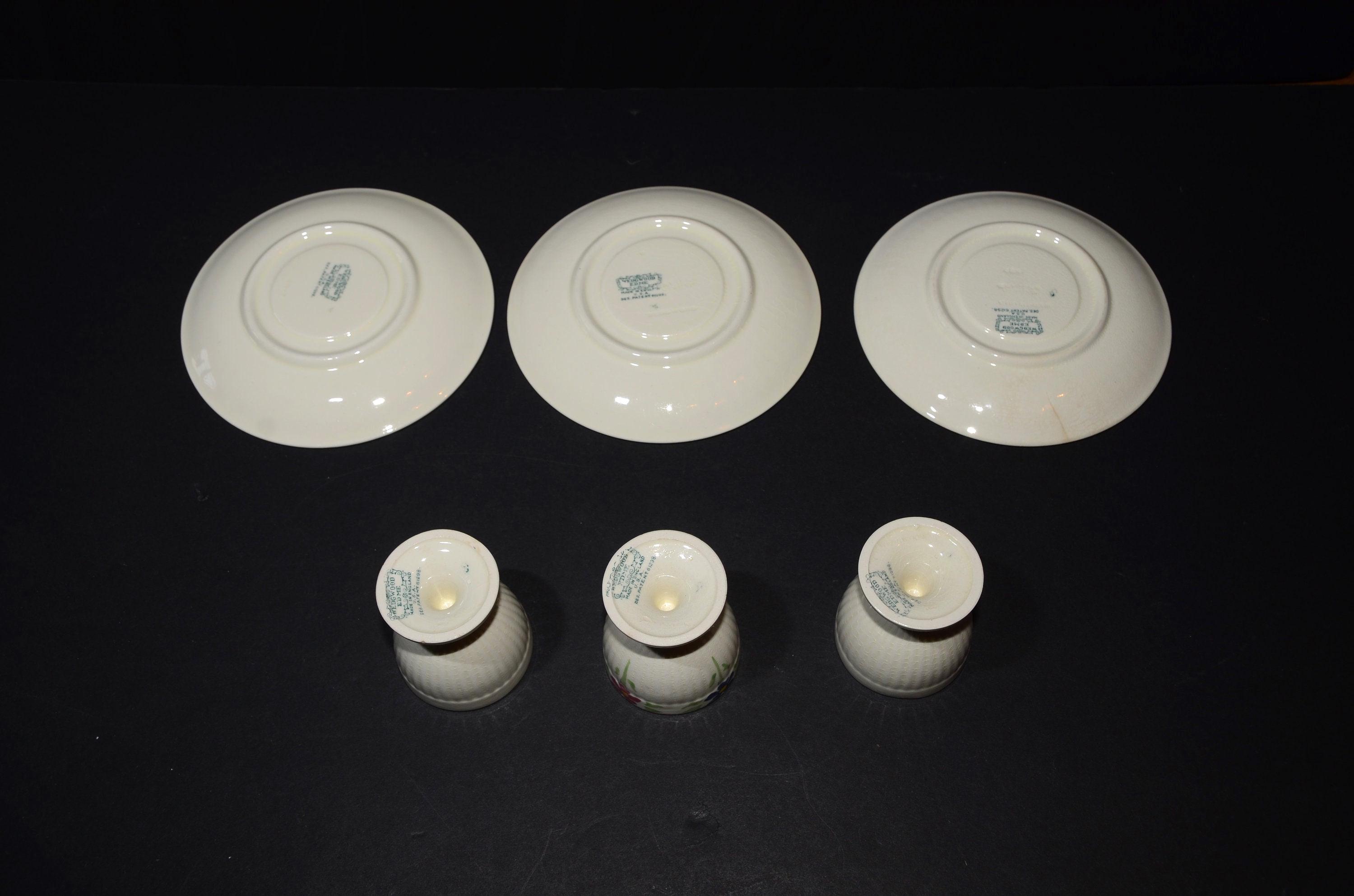 May include: Set of three white ceramic egg cups and three matching saucers with a floral design. The saucers have a raised rim and a blue floral pattern. The egg cups have a similar floral pattern.