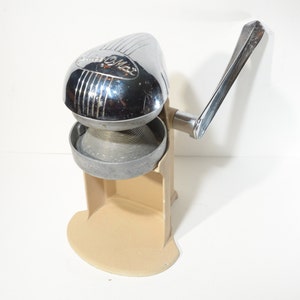 May include: A vintage chrome and beige manual citrus juicer with a lever handle. The juicer has a  "Sunkist" logo on the top.