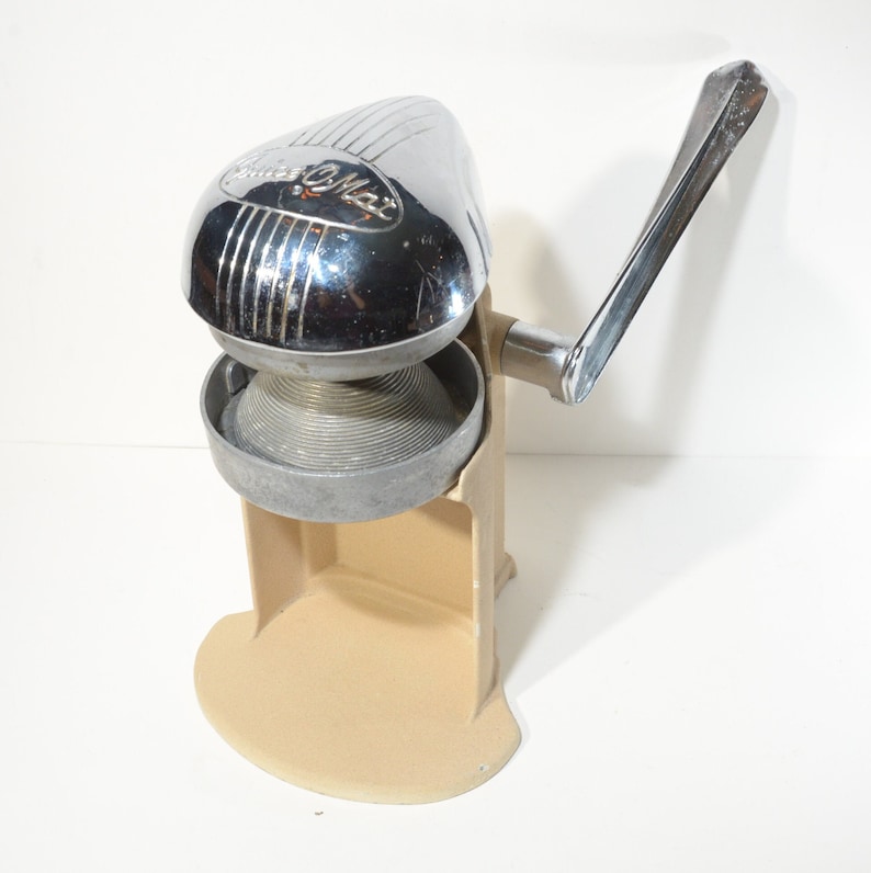 May include: A vintage chrome and beige manual citrus juicer with a lever handle. The juicer has a  "Sunkist" logo on the top.
