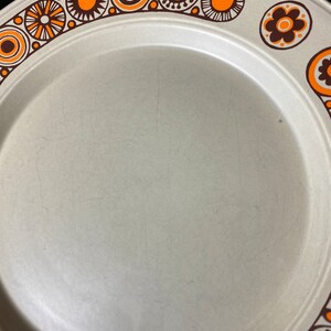 May include: A beige ceramic dinner plate with a brown and orange geometric pattern around the rim.