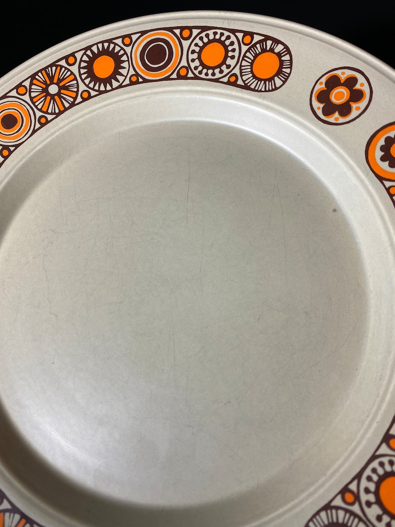 May include: A beige ceramic dinner plate with a brown and orange geometric pattern around the rim.