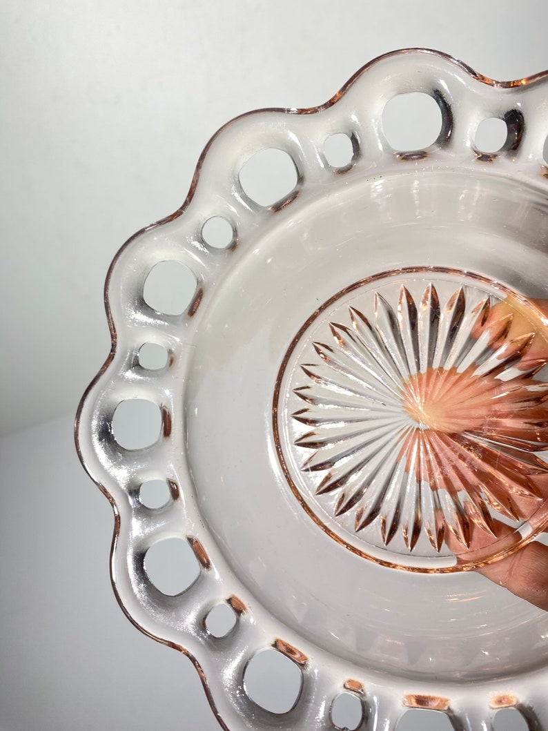 Pode incluir: Um prato de sobremesa de vidro rosa vintage com uma borda festonada e um design de vidro cortado no centro.