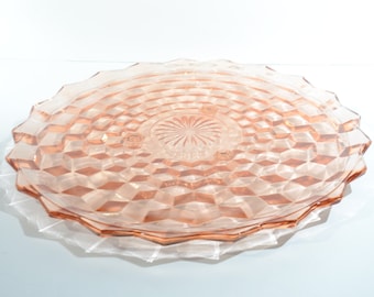 May include: A large, round, pink glass cake plate with a diamond pattern. The plate has three small feet.