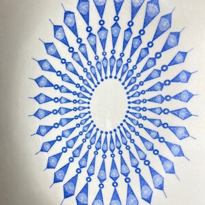 以下が含まれることがあります： 青い幾何学模様が施された白いセラミックボウル。デザインは、円形に配置された一連のダイヤモンドと円を特徴としています。