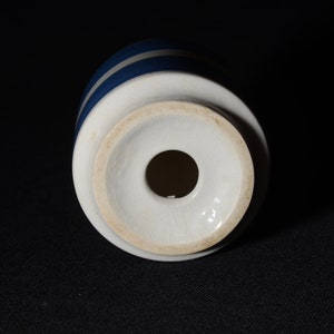 May include: White ceramic bottle stopper with a blue and white striped design. The stopper has a round hole in the center.