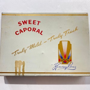 May include: A white rectangular box with gold trim and the text "SWEET CAPORAL Truly Mild - Truly Fresh" in red and gold lettering. The box also features a logo with the text "Finney Bros." in blue cursive lettering.