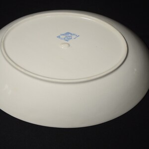 以下が含まれることがあります： 底面に「Samaritan China、Made in Japan、Blue Chip」と書かれた青と白のひし形マークが付いた白い楕円形のサービングプレートです。