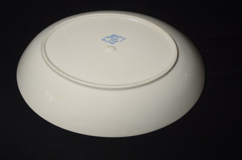 以下が含まれることがあります： 底面に「Samaritan China、Made in Japan、Blue Chip」と書かれた青と白のひし形マークが付いた白い楕円形のサービングプレートです。