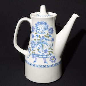 May include: White ceramic coffee pot with a floral design featuring a blue and green stylized woman in a dress. The pot has a spout and a handle.