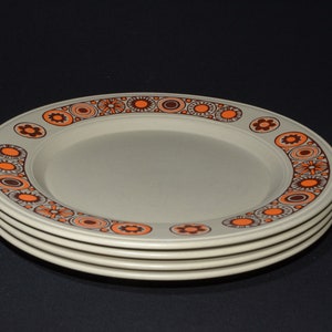 May include: Four beige dinner plates with a brown and orange geometric pattern around the rim.
