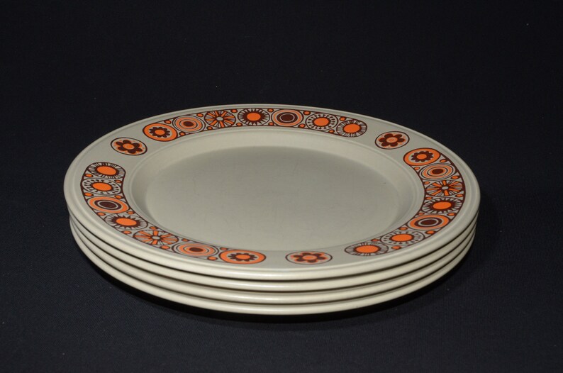 May include: Four beige dinner plates with a brown and orange geometric pattern around the rim.
