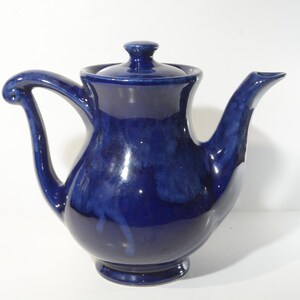 May include: A cobalt blue ceramic teapot with a rounded body and a curved handle. The teapot has a lid with a knob on top.