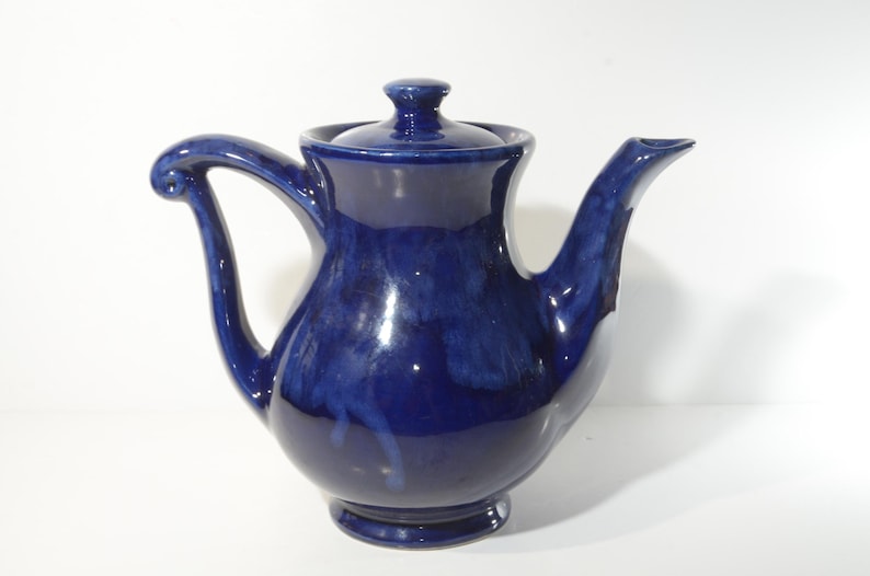 May include: A cobalt blue ceramic teapot with a rounded body and a curved handle. The teapot has a lid with a knob on top.